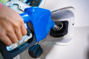 A close-up image shows a gas station attendant's hand holding a blue fuel nozzle, filling a car with gasoline, symbolizing the supply of energy, transportation costs fuel prices, everyday automotive
