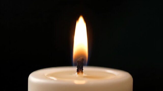Close-up of a hand lighting a white candle wick with a match, creating a warm flame