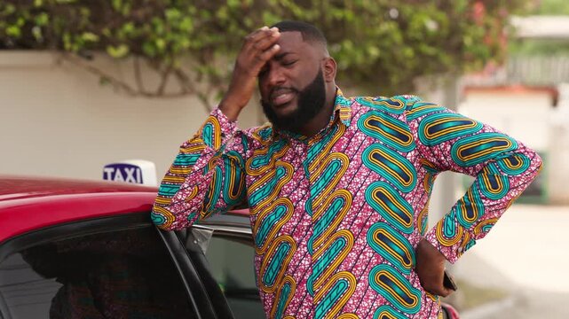 African male taxi driver looking stressed and frustrated while standing by his car in the city