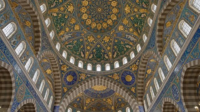 Intricately decorated dome and arched ceiling of a grand building adorned with ornate gold blue and green patterns detailed floral motifs and elegant calligraphy featuring multiple arched windows