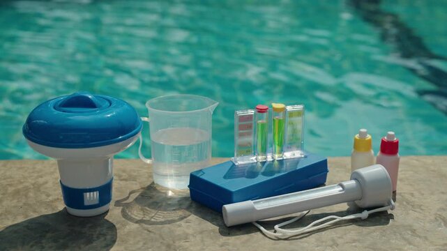 Swimming pool maintenance tools with chlorine dispenser, water test kit, measuring cup and chemical reagents on pool edge, private pool water treatment and quality control 