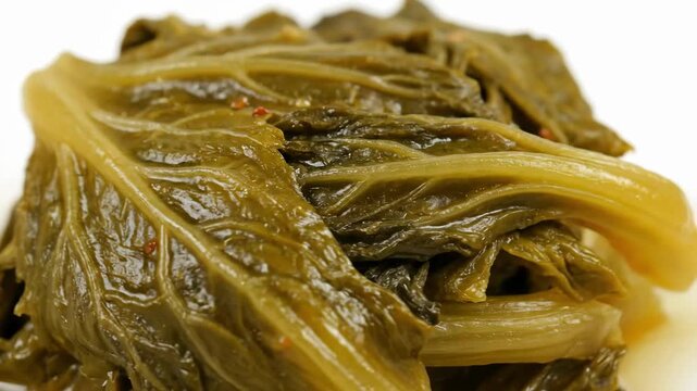 Extreme Close-up of Glossy Braised Leafy Greens (Collard or Mustard Greens) Detailed Macro Food Photography of Seasoned Savory Side Dish Against a White Background.