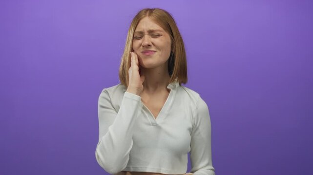 Woman experiencing jaw pain with a concerned expression against an isolated purple background, highlighting her discomfort and emotional distress clearly.