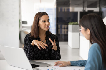 Young Middle Eastern business professional woman talking to consultant, marketing expert, advisor, meeting with colleague at workplace table, discussing analytic report © fizkes