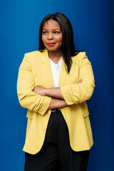 Confident businesswoman smiling with folded arms on blue background