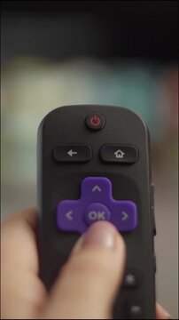 Woman's hand pressing the ok button on a smart tv remote control to select a program on a streaming media player