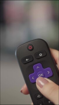 Close-up of a female hand holding a roku remote, navigating through options and pressing the ok button to watch a movie or tv show