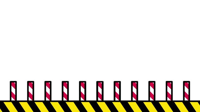 A series of red and white striped bollards are lined up along a yellow base to create a safety fence
