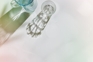 Transparent Water Glasses and water jug with shadows at sunlight on white, pastel color photo minimal style, aesthetic top view shiny cups sparkling at natural light, summer drink, composition