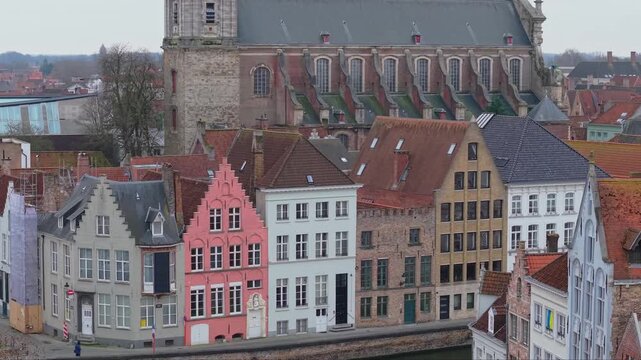 Aerial reveal shot of the baroque St. Walburga&rsquo;s Church rising behind traditional colorful houses along the Bruges canal. Scenic Flemish architecture and historic city landscape in Belgium.