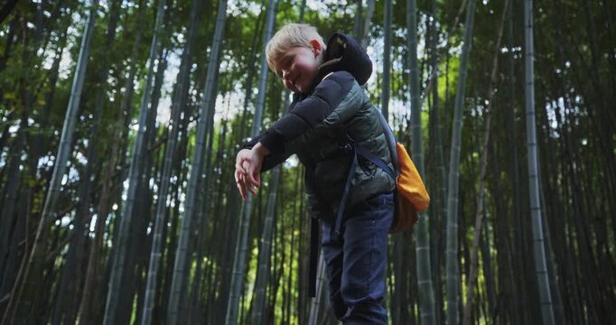 Low shot of little boy standing up in bamboo thicket and putting on backpack