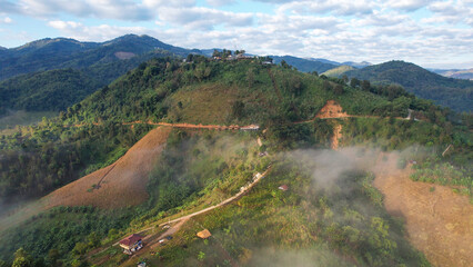 Fototapeta premium Aerial view of the rural village and dirt road in the mountains on foggy morning by drone