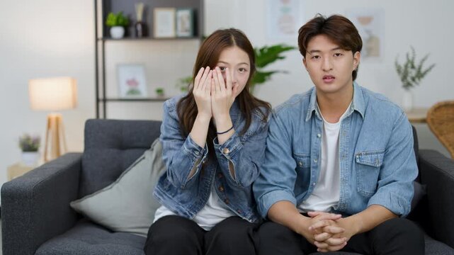 Young Asian Couple Reacting with Fear While Watching Horror Movie at Home