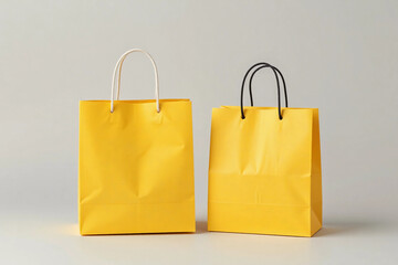 Two bright yellow paper shopping bags with black handles on grey background