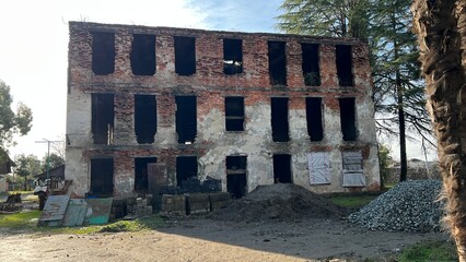The exterior of an abandoned, dilapidated red brick building with three floors and empty window openings.