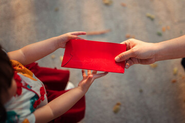 Top view Close-up of adult hands giving a red envelope (Angpao) to a little girl in traditional Chinese dress. Lunar New Year celebration cultural tradition and family blessing
