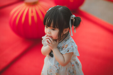 Cute Asian toddler girl in white traditional Qipao looking curious and innocent. Chinese New Year celebration and cultural tradition concept. Happy little child in festive costume with red lanterns