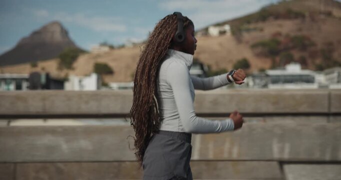 Running, check watch and black woman with headphones in city for fitness, timer or cardio health. Music, jog and person with wristwatch for workout tracking, exercise or listen to audio on bridge