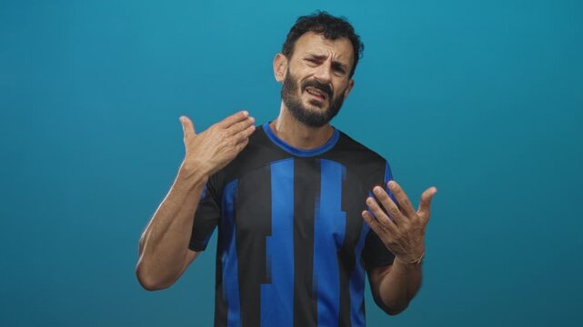 Man in soccer uniform gesturing with open hands and visible beard, palms out, expressive face in studio; frustration.