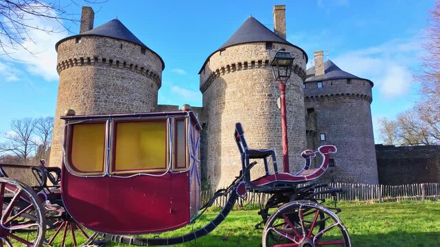 Cal&egrave;che or vintage red horse-drawn carriage, parked on the grass in front of the stone walls of medieval Lassay castle in Lassay-les-chateaux, Mayenne in France