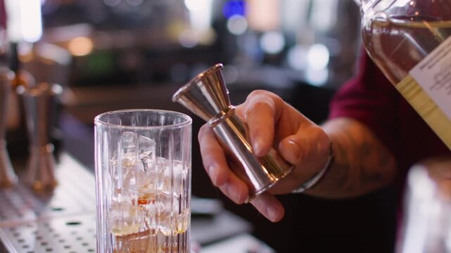 Cocktail recipe. Making beverage mix. Bartender hand pouring sweet aroma color syrup from metal jigger to glass. Flavored refreshing drink.