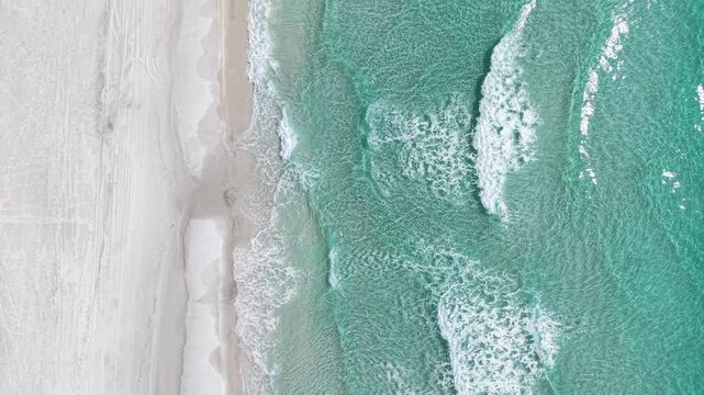Top-down drone fly over a beautiful sandy shoreline meeting crystal clear Gulf waves, 30A, Florida, USA