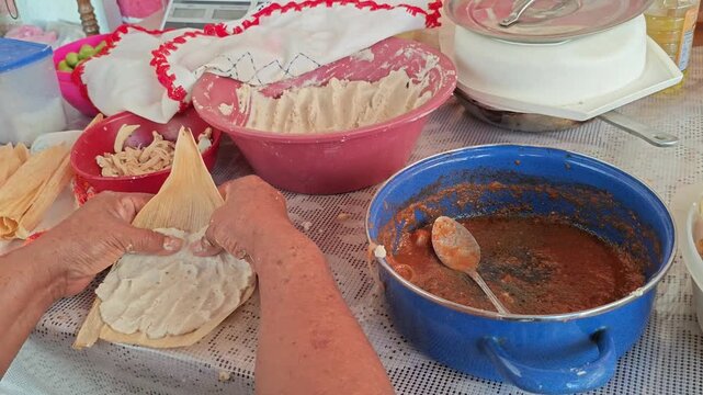 Close-up of hands spreading masa dough on a corn husk for tamales