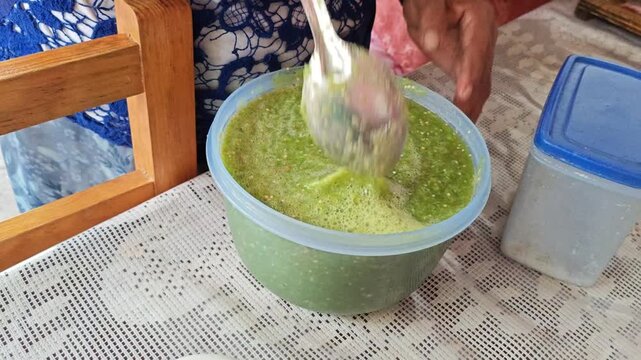 Stirring fresh green Mexican salsa in a plastic container with a spoon.