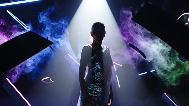 Woman in colorful dress standing under spotlight with abstract shapes and smoke in background, representing artistic or creative performance