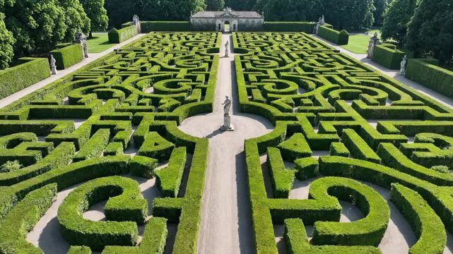 Aerial view of intricate green hedge maze in a serene formal garden setting with statue and pathway