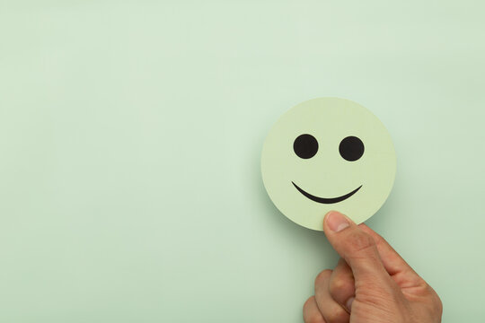Hand holding a green smiley face over a pastel background. Concept for customer satisfaction, mental health awareness, positive feedback, wellness, and business growth with copy space for text.