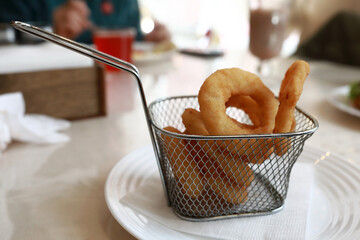 Golden fried onion rings in a metal serving basket
