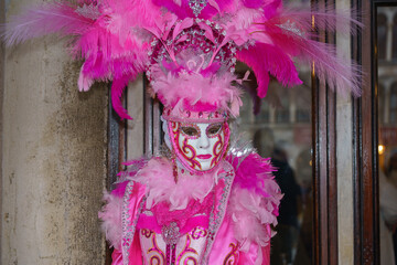 Close-up portrait of Venetian carnival performer in bright pink costume with feathers and decorative mask
