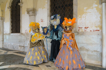 Three performers in elaborate Venetian carnival costumes pose under historic arcade in Venice