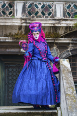 Full-length portrait of Venetian carnival performer wearing vibrant blue and magenta baroque costume with decorative fan and birds details