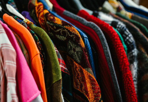 Thrifted vintage shirts of many colors and patterns on a clothing rack in a shop