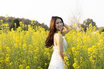 Fototapeta premium Happy asian woman in yellow flower field enjoying nature outdoor during summer. beautiful portrait of young lady smiling with joy in countryside sunshine