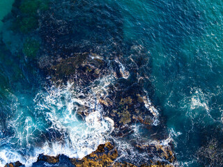 Obraz premium Turquoise water with reef. Blue ocean water. Coastline from above. Summer beach with crashing waves. Dramatic coastline. Ocean surface. Rocky coast with sea foam. Wave moving.