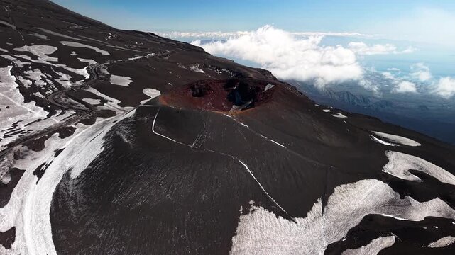 Mount Etna aerial view rising above the volcanic crater and snow covered black fertile mountain soil