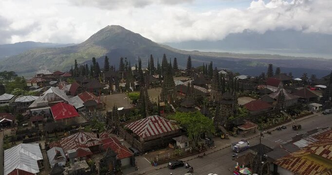 Aerial drone clip flying forward toward Pura Besakih Temple, the mother temple of Bali, with Mount Agung volcano rising in the background, showing traditional architecture and daily life in Bali, Indo
