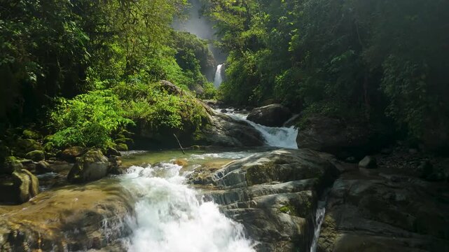 FPV style aerial view flying low under a bridge and following the rushing mountain river downstream from Cascada El Rocio Machay through a lush tropical canyon