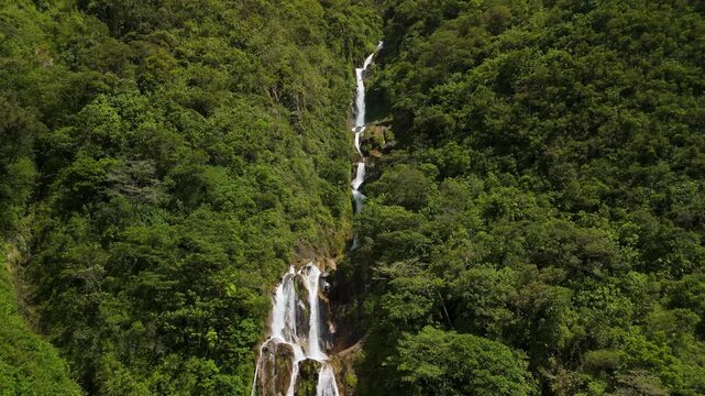 Dynamic aerial parallax shot revealing Cascadas Chamana waterfall hidden within dense tropical forest on mountain slope under soft light in Banos Ecuador
