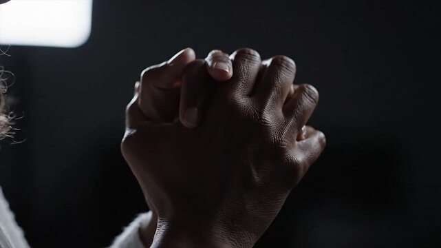 Close up of hands clasped in prayer against a dark background.