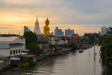 Wat Paknam Phasi Charoen, Thailand, majestic Big Buddha rising above the Bangkok skyline at sunset. Long-tail boat moves along canal. Big Buddha of Wat Paknam Phasi Charoen stands as a  landmark. © Hathaichanok