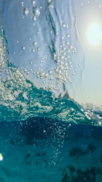 Vertical half underwater view of big waves and anchored diving yacht near coral reef in red sea
