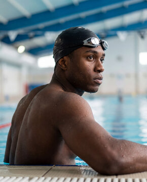 Portrait of a Focused Young Black Male Swimmer Resting at the Edge of an Indoor Pool