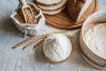 Fresh wheat and flour rest on the table, accompanied by sliced bread and a scoop, ready for baking