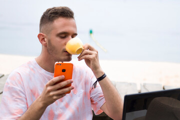 Fototapeta premium A young man checks his phone at a beach bar while drinking coffee.