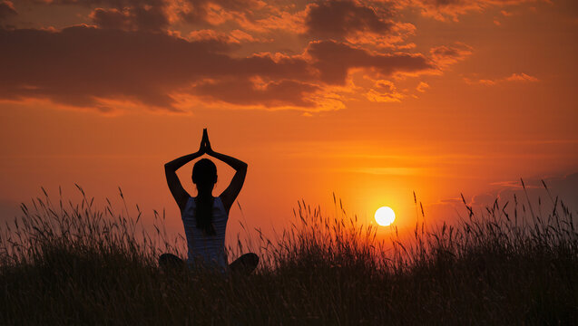 Yoga silhouette in Anjali Mudra at sunset, surrounded by tall grass, with warm orange and red skies, evoking serenity, mindfulness, and spiritual calm.