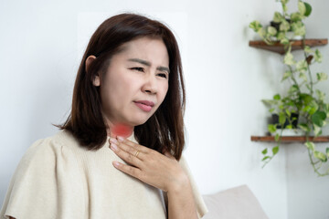 Asian middle-aged woman suffering from acid reflux or GERD symptoms. Mature female holding her throat with red pain area, feeling chest burn and discomfort from gastroesophageal reflux 